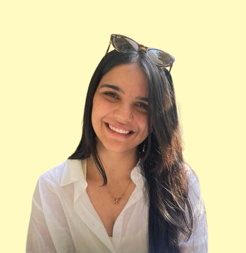 A headshot of Shalini smiling into the camera against a solid yellow background.